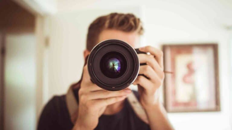 A person with short hair is holding a camera with a large lens, taking a photo indoors.