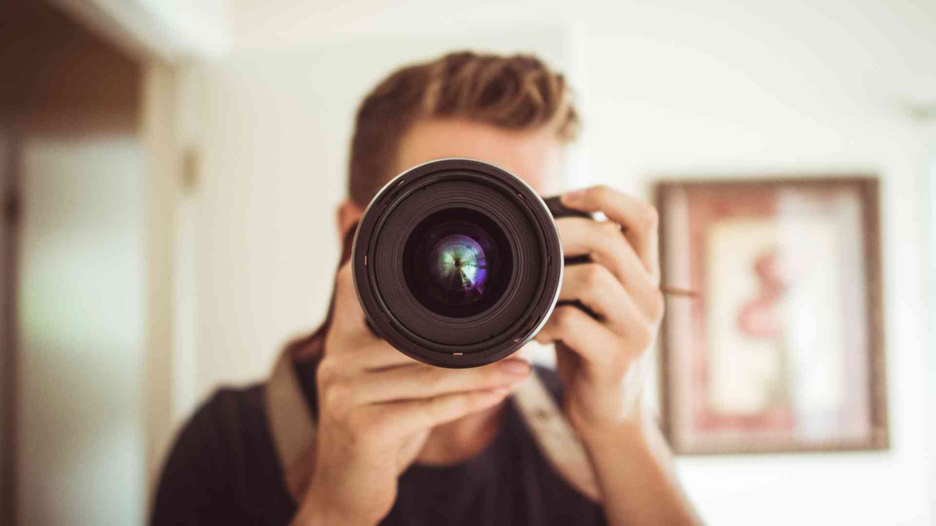 A person with short hair is holding a camera with a large lens, taking a photo indoors.