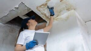 woman inspecting ceiling for signs of water damage after wet spots occur in home
