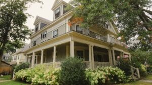 mid-century modern farmhouse with wrap-around porch and green bushes and foliage in front