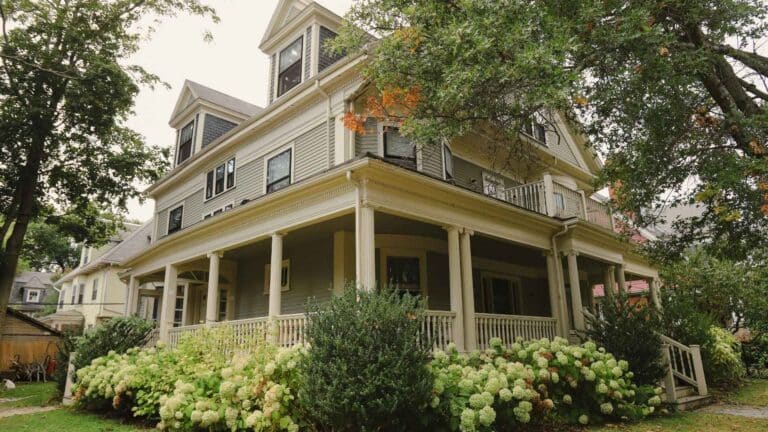 mid-century modern farmhouse with wrap-around porch and green bushes and foliage in front