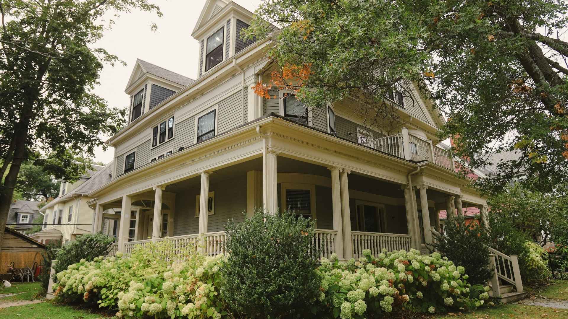 mid-century modern farmhouse with wrap-around porch and green bushes and foliage in front
